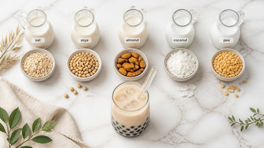 Five labelled jugs of oat, soya, almond, coconut and pea milk with their raw ingredients and a milk tea