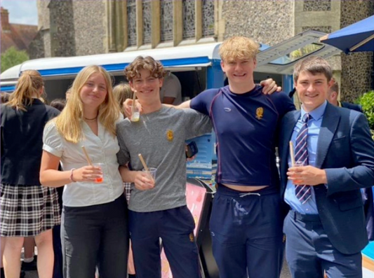 Young people and staff holding cups of bubble tea beside a drinks van outside a stone building