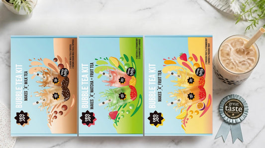 TeaJoy's three bubble tea kits, Milk Tea, Matcha and Fruit Tea, beside a milk bubble tea with tapioca pearls and a rosette
